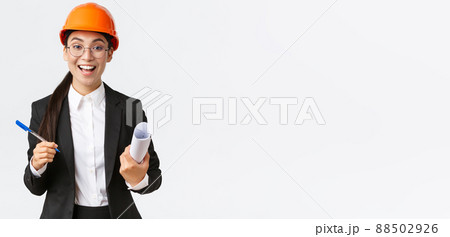 Smiling professional female architect, asian engineer in helmet and business suit, holding blueprints and pen, siging contract, making deal with investors at construction area, white background 88502926