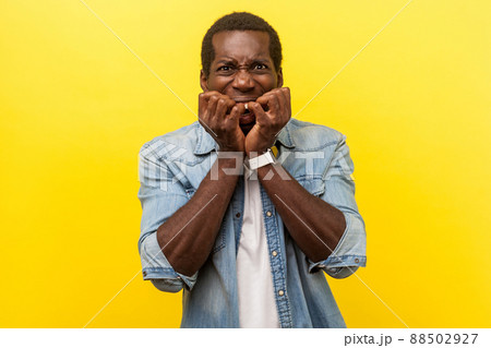Portrait of panicked young man in denim casual shirt with rolled up sleeves biting nails feeling anxious and terrified about problems, stress at work. indoor studio shot isolated on yellow background 88502927