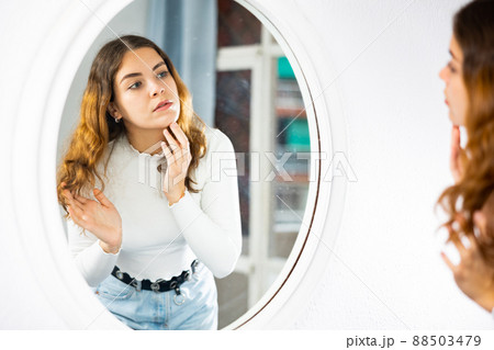 Young woman looking at face in mirror 88503479