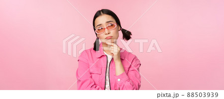 Portrait of sad and gloomy asian girl sulking from disappointment, standing upset against pink studio background Portrait of sad and gloomy asian girl sulking from disappointment, standing upset against pink studio background 88503939