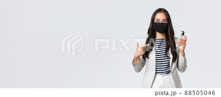 Business, finance and employment, covid-19 preventing virus and social distancing concept. Smiling cute asian office worker in face mask recommend using hand sanitizer while at work Business, finance and employment, covid-19 preventing virus and social distancing concept. Smiling cute asian office worker in face mask recommend using hand sanitizer while at work 88505046
