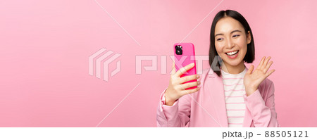 Stylish asian businesswoman, girl in suit taking selfie on smartphone, video chat with mobile phone app, posing against pink studio background 88505121