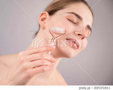 Close-up portrait of a woman using a quartz roller massager on her cheek for an alternative anti-aging. Close-up portrait of a woman using a quartz roller massager on her cheek for an alternative anti-aging. 88505801