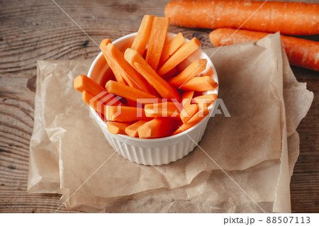 cut slices of carrots in a white bowl, on a wooden background. Vegetable snacks. 88507113