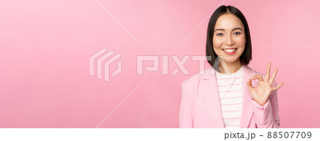 Excellent work, well done gesture. Smiling asian businesswoman showing okay, ok sign, praise good work, recommending company, looking as confident professional, pink background 88507709
