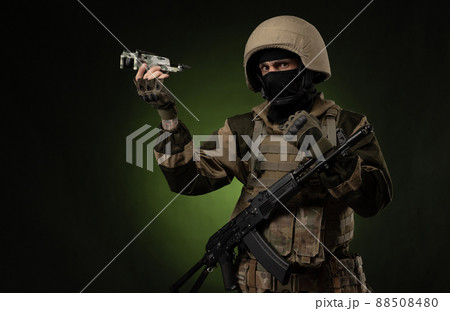 a soldier in military clothes with a weapon launches a small unmanned quadcopter for reconnaissance on a dark background a soldier in military clothes with a weapon launches a small unmanned quadcopter for reconnaissance on a dark background 88508480