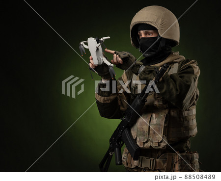 a soldier in military clothes with a weapon launches a small unmanned quadcopter for reconnaissance on a dark background 88508489