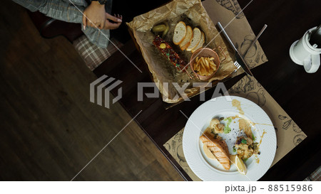 Woman is sitting at a wooden dining wooden table in a restaurant with fish tartare and baked fish fillet with vegetables. Lunch break. Great seafood snacks Woman is sitting at a wooden dining wooden table in a restaurant with fish tartare and baked fish fillet with vegetables. Lunch break. Great seafood snacks 88515986
