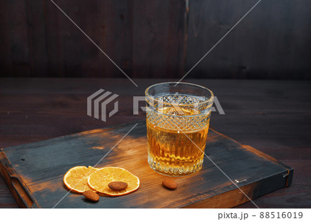 Delicious amazing Scotch whiskey in a crystal glass decorated with slices of fresh orange stands on a vintage wooden table in the pub. Strong male drink. Weekend at the bar Delicious amazing Scotch whiskey in a crystal glass decorated with slices of fresh orange stands on a vintage wooden table in the pub. Strong male drink. Weekend at the bar 88516019