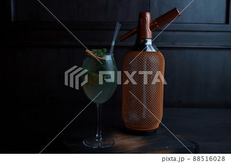 Amazing alcoholic cocktail in an elegant glass with tequila with vanilla syrup and fresh mint leaves stands on a vintage table in a bar near a golden luxury bottle. Drink with orange slices. Close-up 88516028
