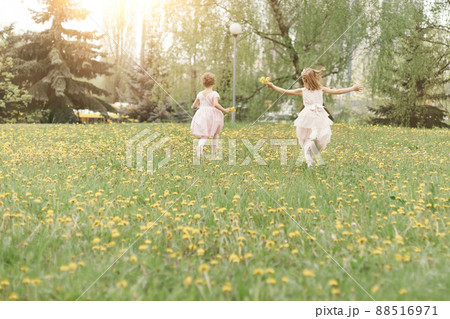 two little sisters running across the lawn on a spring day . 88516971