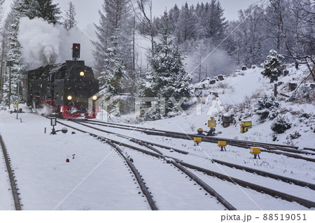 Steam locomotive with smoking and steaming chimney is heading for the snowy switches of the tracks in the forest in winter time 88519051