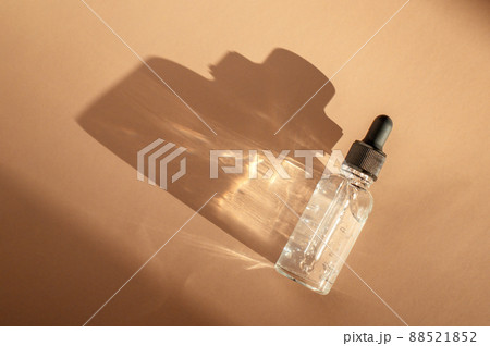 Transparent glass dropper bottle with air bubbles on beige background in sunlight. Pipette with fluid hyaluronic acid, serum, retinol. Cosmetics and healthcare concept Flat lay. Luxury beauty product 88521852