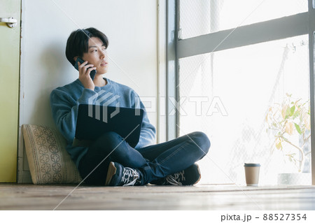 パソコンを見ながら電話する若い男性 パソコンを見ながら電話する若い男性 88527354