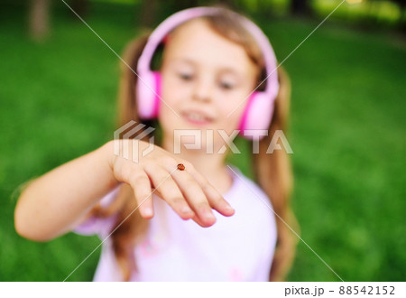 a child - a little girl in pink headphones looks at a ladybug on her hand. 88542152