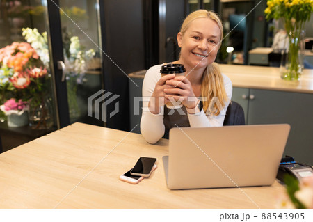 a salesman in a flower shop works at a computer with a cup of coffee in his hands and looks at the a salesman in a flower shop works at a computer with a cup of coffee in his hands and looks at the 88543905