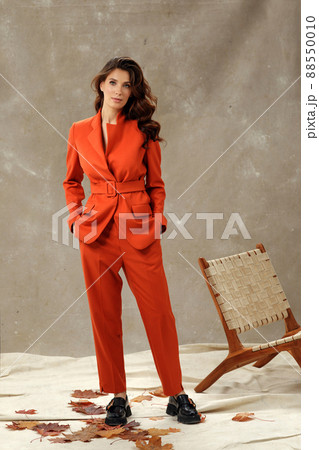 Studio portrait of self confident young female fashion model with long wavy hair in trendy business clothes in orange tones. Collection of comfortable business clothes. Fall concept studio shot 88550010