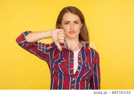 Dislike. Portrait of dissatisfied unhappy ginger girl in red shirt showing thumb down gesture and looking displeased, negative feedback, disapproval sign. studio shot isolated on yellow background 88550330