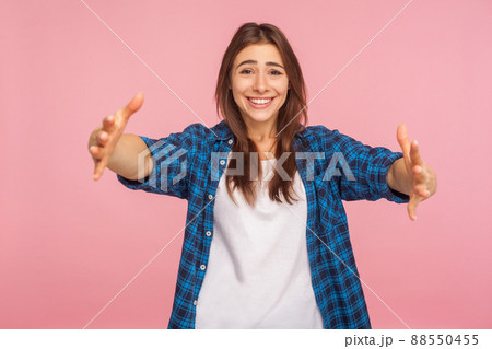 Let me embrace you. Portrait of kind-hearted girl in checkered shirt opening her arms wide to hug you, welcoming with toothy smile, sharing love. indoor studio shot isolated on pink background Let me embrace you. Portrait of kind-hearted girl in checkered shirt opening her arms wide to hug you, welcoming with toothy smile, sharing love. indoor studio shot isolated on pink background 88550455