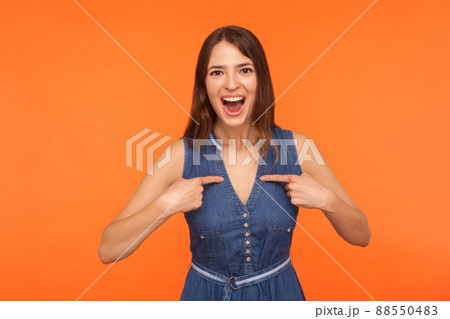 Wow, look at me. Excited amazed brunette woman in denim dress pointing herself with amazed shocked expression, feeling surprised and proud about success. studio shot isolated on orange background 88550483