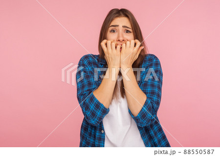 Anxiety. Portrait of scared girl in checkered shirt biting nails fingers and looking terrified, having depression and nervous problem, panic attack. indoor studio shot isolated on pink background 88550587