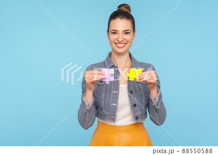 Fascinating joyful fashionably dressed woman with hair bun holding colorful pieces of puzzle, two parts of one, symbol of connection and union, association. studio shot isolated on blue background 88550588