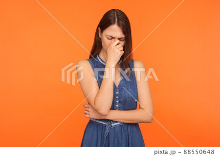 Frustrated sad brunette woman in denim dress crying, wiping away tears, feeling depressed helpless, upset about loss, bereavement, desperate emotions. indoor studio shot isolated on orange background 88550648