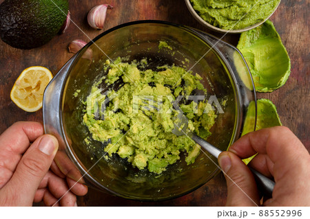 Man's hands mashing several avocados in a bowl with a fork to prepare a rich and fresh guacamole. Ingredients in composition on a wooden background in brown tones. Healthy food concept Man's hands mashing several avocados in a bowl with a fork to prepare a rich and fresh guacamole. Ingredients in composition on a wooden background in brown tones. Healthy food concept 88552996