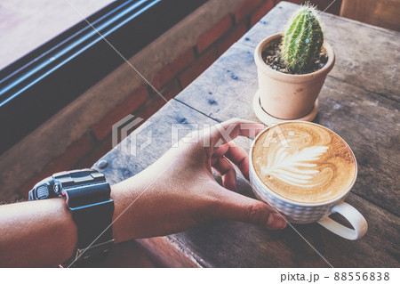 Shot of men's hand touching a cup of hot milk coffee (Latte coffee or Cappuccino coffee) on the wooden table in coffee shop. 88556838