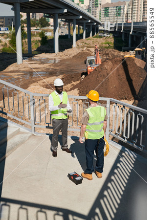 Backlit side view at two construction workers discussing project while standing at high rise building, copy space 88565549