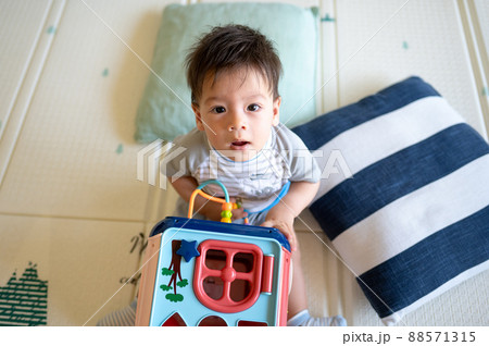 Baby boy playing with activity box in the bedroom while sitting on the floor 88571315