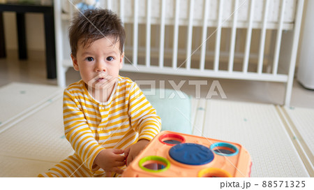 Baby boy playing with activity box in the bedroom while sitting on the floor wearing yellow pajama Baby boy playing with activity box in the bedroom while sitting on the floor wearing yellow pajama 88571325