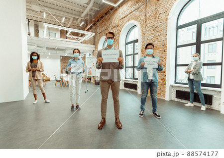 Colleagues in face masks holding sheets of paper with inscriptions Colleagues in face masks holding sheets of paper with inscriptions 88574177