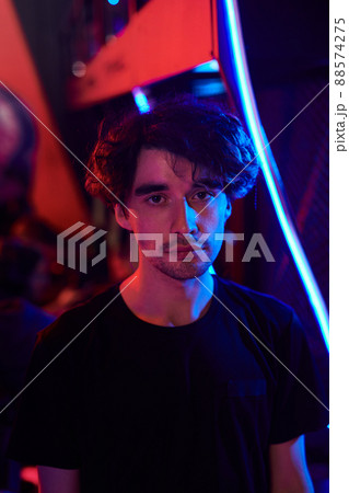 Portrait of sad young Caucasian man in black tshirt standing in esports bar, blue and red lights 88574275