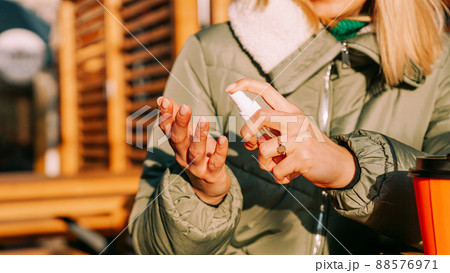 A young woman in a warm jacket treats her hands with an antiseptic outside. 88576971