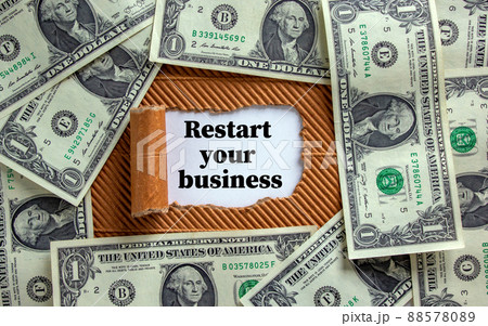 The text 'restart your business' appearing behind torn brown paper. Dollar bills. Business concept. The text 'restart your business' appearing behind torn brown paper. Dollar bills. Business concept. 88578089