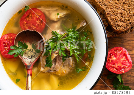 fish soup with carp, potatoes, parsley, tomato in enamel bowl stands on a board fish soup with carp, potatoes, parsley, tomato in enamel bowl stands on a board 88578592