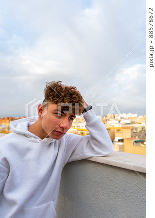 Portrait of smiling young Caucasian man with curly hair dressed in a white sweatshirt looking at the camera with the city skyline in the background Portrait of smiling young Caucasian man with curly hair dressed in a white sweatshirt looking at the camera with the city skyline in the background 88578672