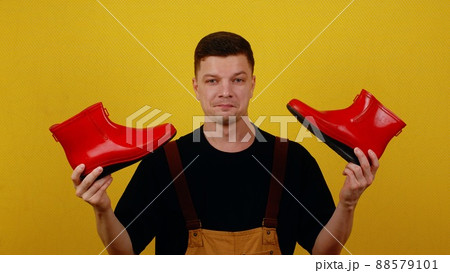 A gardener in overalls holds bright red boots in his hands. The concept of the beginning of the gardening season 88579101