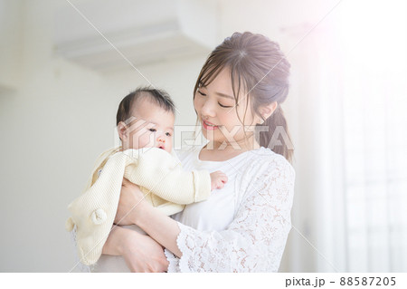 明るいリビングで赤ちゃんを抱っこしあやすお母さん 88587205