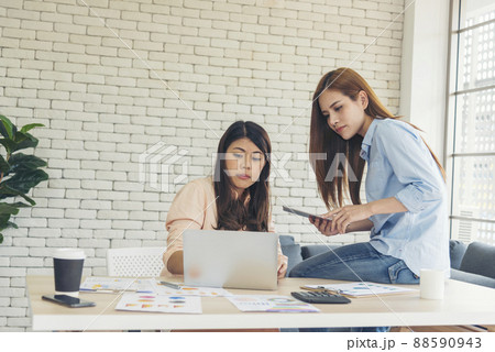 Happiness two women working together confident team meeting in office desk. Team business partners working with computer laptop startup company. Asian colleague friendship at work with smiling face. 88590943