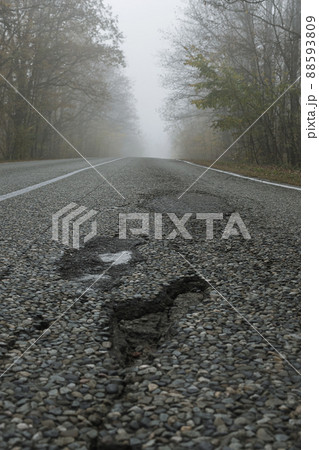 Potholes on a paved road. Nearby you can see traces of repairing another pothole. Bad condition of the country road. Broken road in the foggy forest. Potholes on a paved road. Nearby you can see traces of repairing another pothole. Bad condition of the country road. Broken road in the foggy forest. 88593809