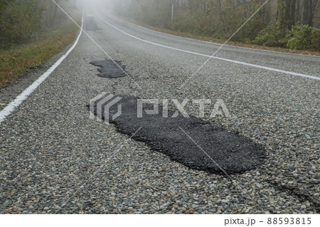 Fresh patches after patching the road. Country highway in the foggy forest. Bad road condition. 88593815