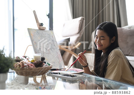 Joyful asian girl sitting in living room and painting picture with watercolor. Joyful asian girl sitting in living room and painting picture with watercolor. 88593862