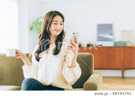ソファに座ってコーヒーを飲みながらスマホを見る女性 ソファに座ってコーヒーを飲みながらスマホを見る女性 88594762