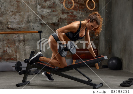 Gorgeous brunette lifting some weights and training her biceps in a gym. 88598251