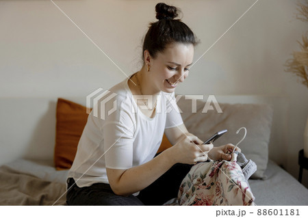 Young woman sitting on the bed at home and taking photo of her old clothes to sell them online. Selling on website, e-commerce. Reuse, second-hand concept. Conscious consumer, sustainable lifestyle. Young woman sitting on the bed at home and taking photo of her old clothes to sell them online. Selling on website, e-commerce. Reuse, second-hand concept. Conscious consumer, sustainable lifestyle. 88601181