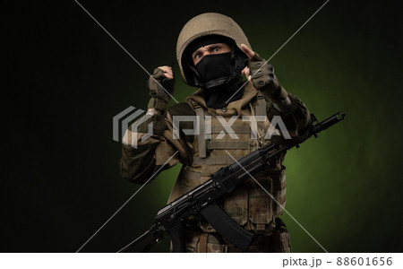 a Russian soldier in military clothes with a Kalashnikov assault rifle on a dark background takes orders on a walkie-talkie a Russian soldier in military clothes with a Kalashnikov assault rifle on a dark background takes orders on a walkie-talkie 88601656