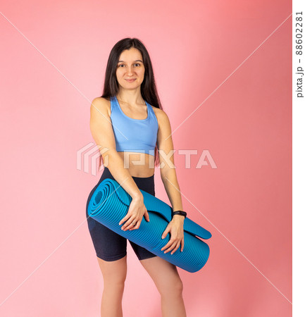 Attractive brunette woman in fashionable sportswear on pink background. Sport Girl with mat after gum. Healthy lifestyle concept 88602281