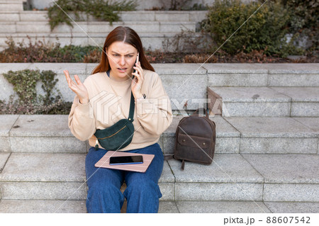 Upset young woman talking over phone disappointed hear bad news, sad pensive girl speaking having unpleasant smartphone conversation and siting on stairs on city street. Negative emotion Upset young woman talking over phone disappointed hear bad news, sad pensive girl speaking having unpleasant smartphone conversation and siting on stairs on city street. Negative emotion 88607542